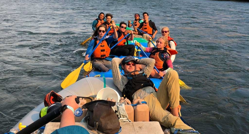 a group of outward bound students wearing life jackets take a rest in their rafts on calm water